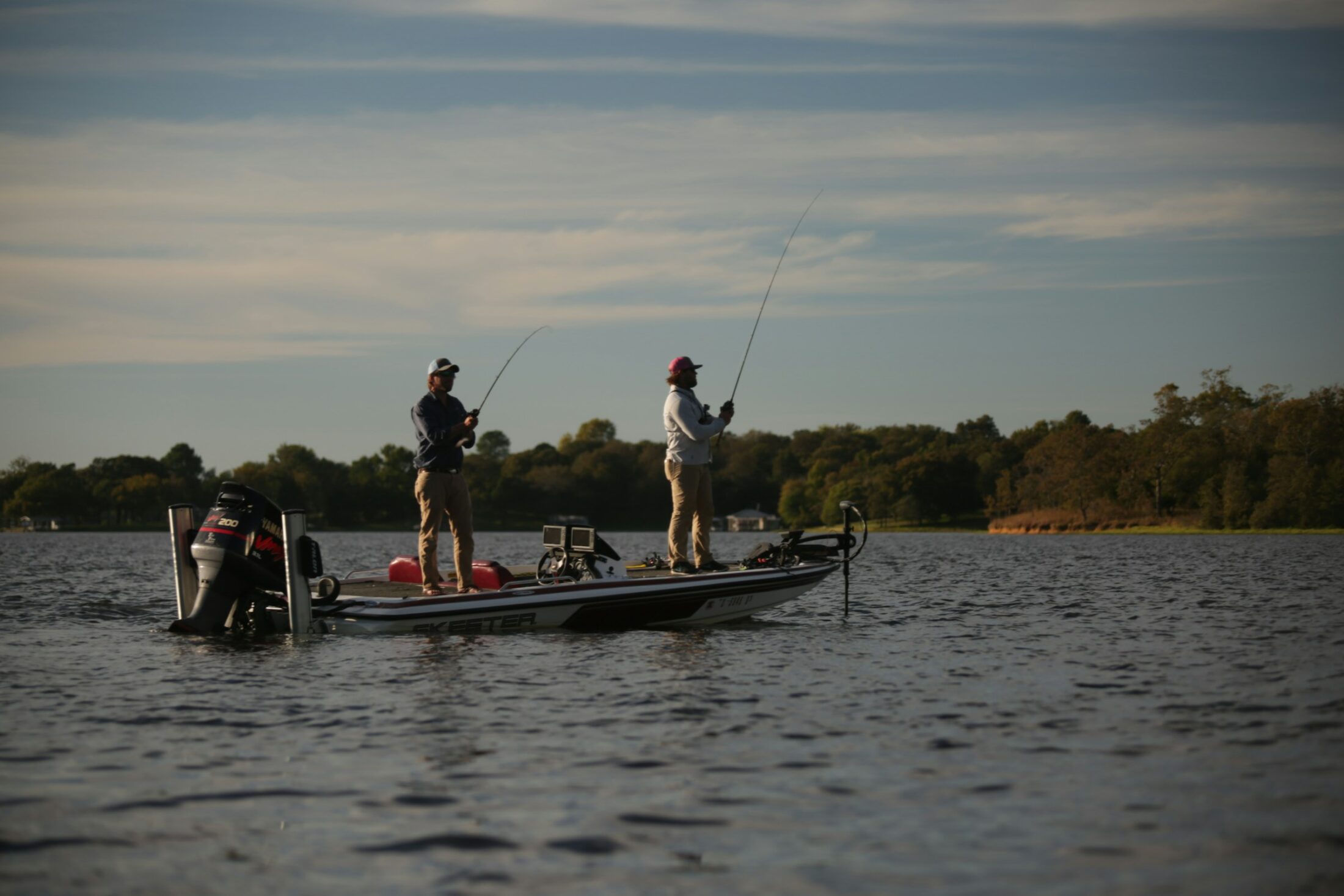 Anglers casting from a bass boat on a lake in fall light