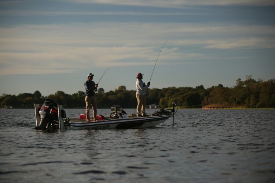 Anglers casting from a bass boat on a lake in fall light